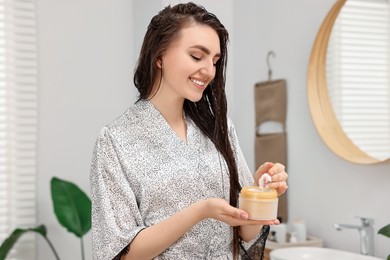 Photo of Young woman with jar of hair mask in bathroom