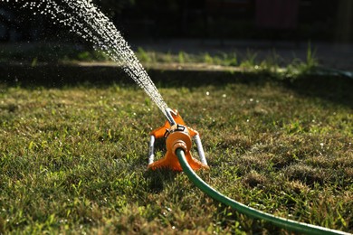 Photo of Automatic sprinkler watering green grass on sunny day outdoors. Irrigation system