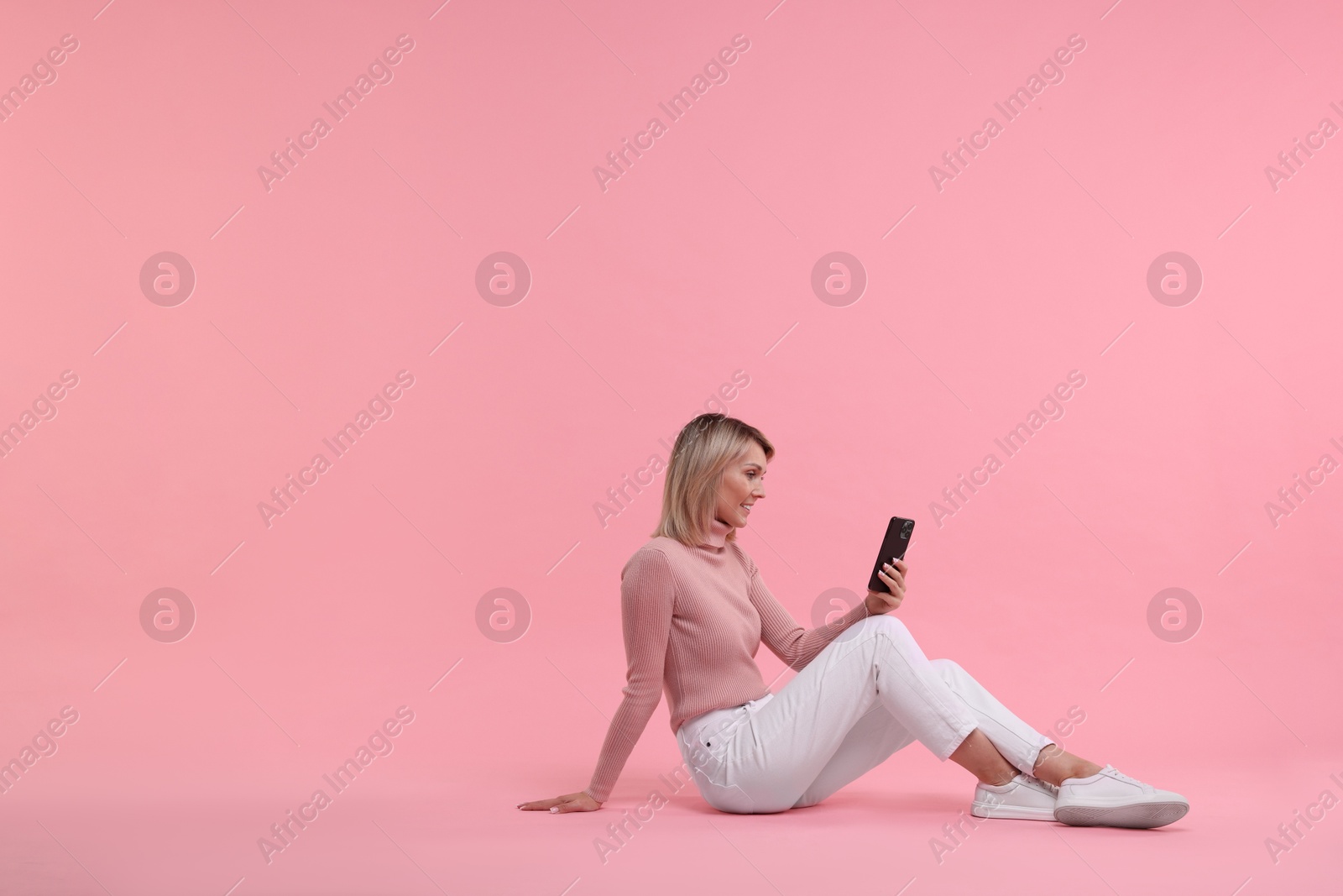 Photo of Happy woman with phone on pink background, space for text