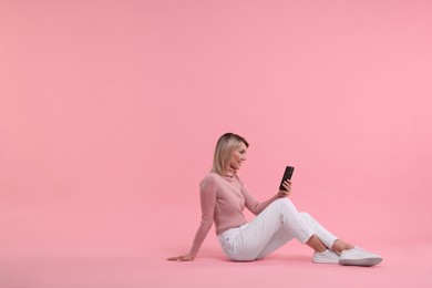 Photo of Happy woman with phone on pink background, space for text