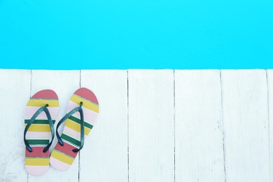 Photo of Slippers on wooden deck near swimming pool, top view with space for text. Beach accessory