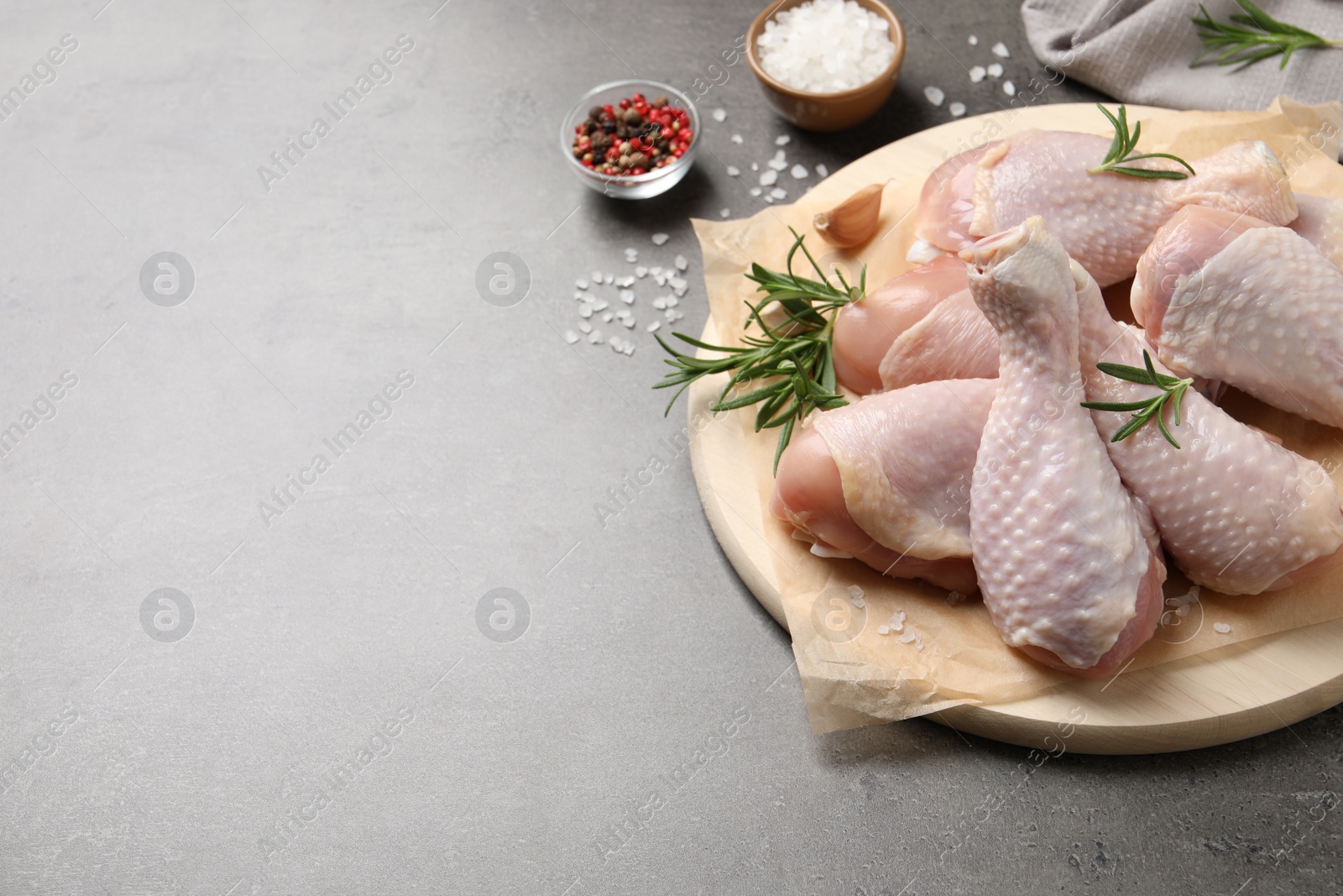 Photo of Wooden board with fresh raw chicken legs and other products on grey table. Space for text