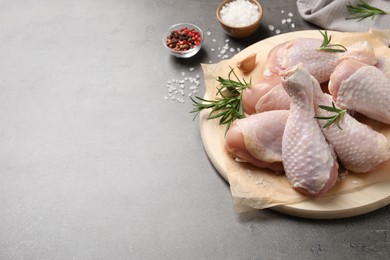 Photo of Wooden board with fresh raw chicken legs and other products on grey table. Space for text