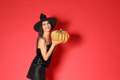 Photo of Beautiful young woman wearing witch costume with pumpkin for Halloween party on red background, space for text