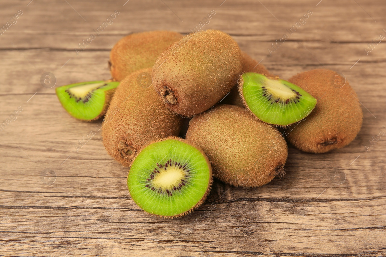 Photo of Heap of whole and cut fresh kiwis on wooden table