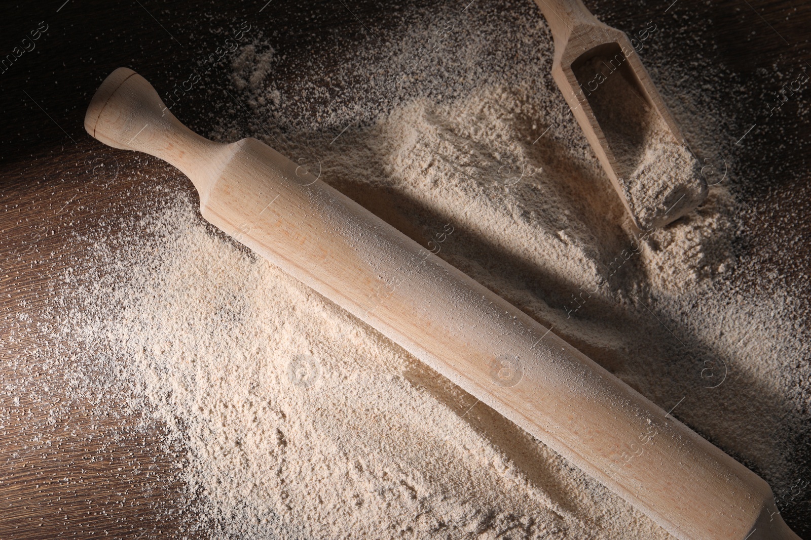 Photo of Pile of flour, rolling pin and scoop on wooden table, flat lay