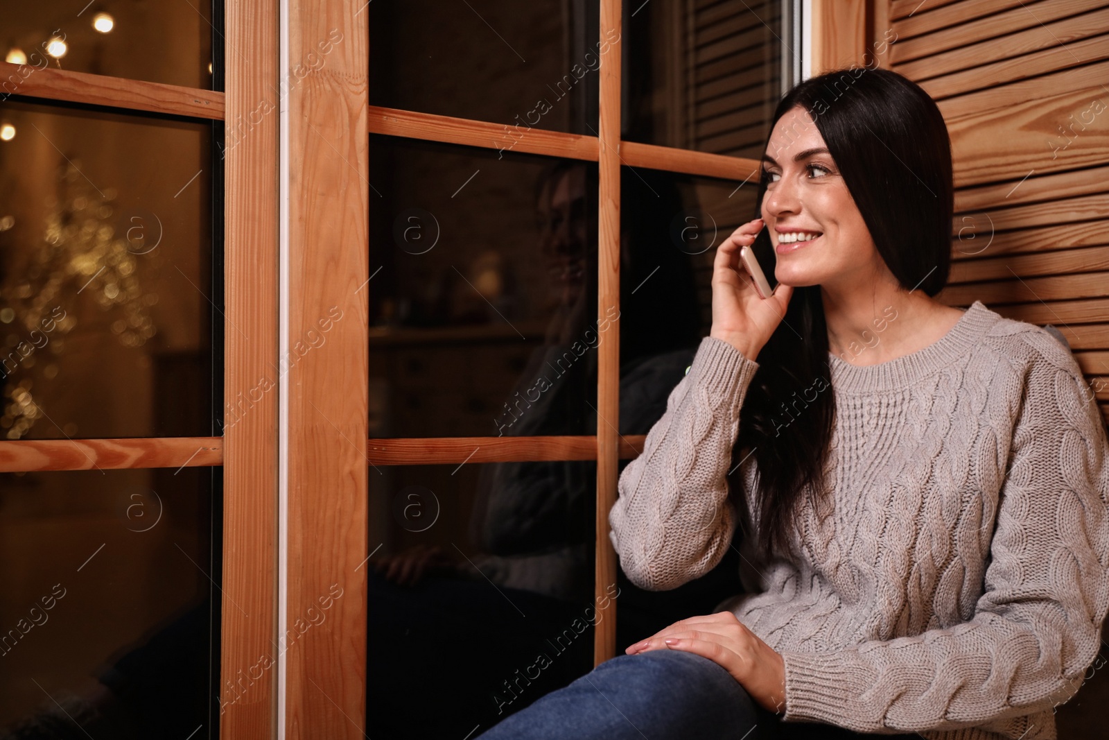 Photo of Beautiful woman talking on mobile phone near window indoors. Christmas celebration