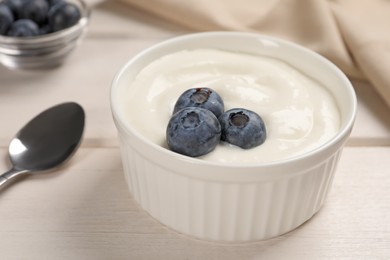 Photo of Bowl of yogurt with blueberries served on white wooden table, closeup