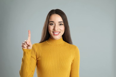 Photo of Woman in yellow turtleneck sweater showing number one with her hand on grey background