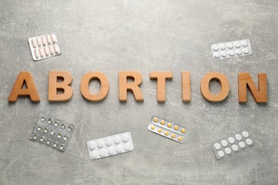 Photo of Word Abortion made of wooden letters and pills on grey background, flat lay