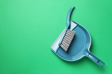 Plastic hand broom and scoop on green background, flat lay. Space for text