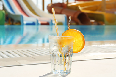 Glass of refreshing drink near swimming pool