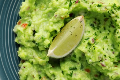 Photo of Delicious guacamole served with lime on plate, top view