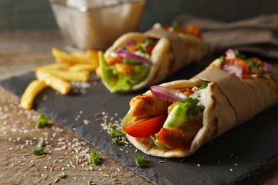 Delicious pita wraps with meat, vegetables and potato fries on wooden table, closeup. Space for text