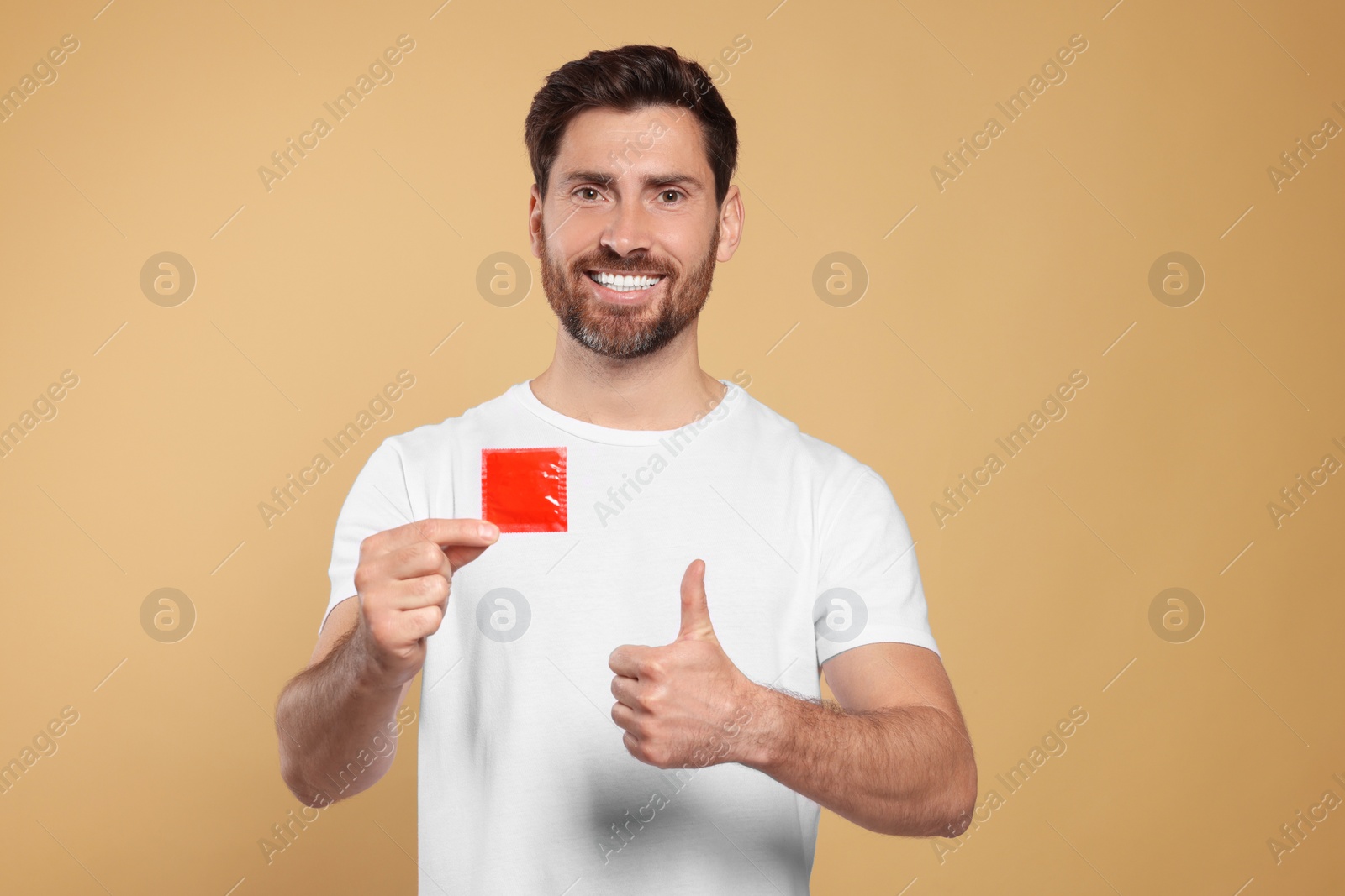 Photo of Happy man with condom showing thumb up on beige background. Safe sex