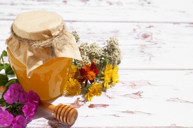 Photo of Glass jar of honey, dipper and different flowers on white wooden table. Space for text