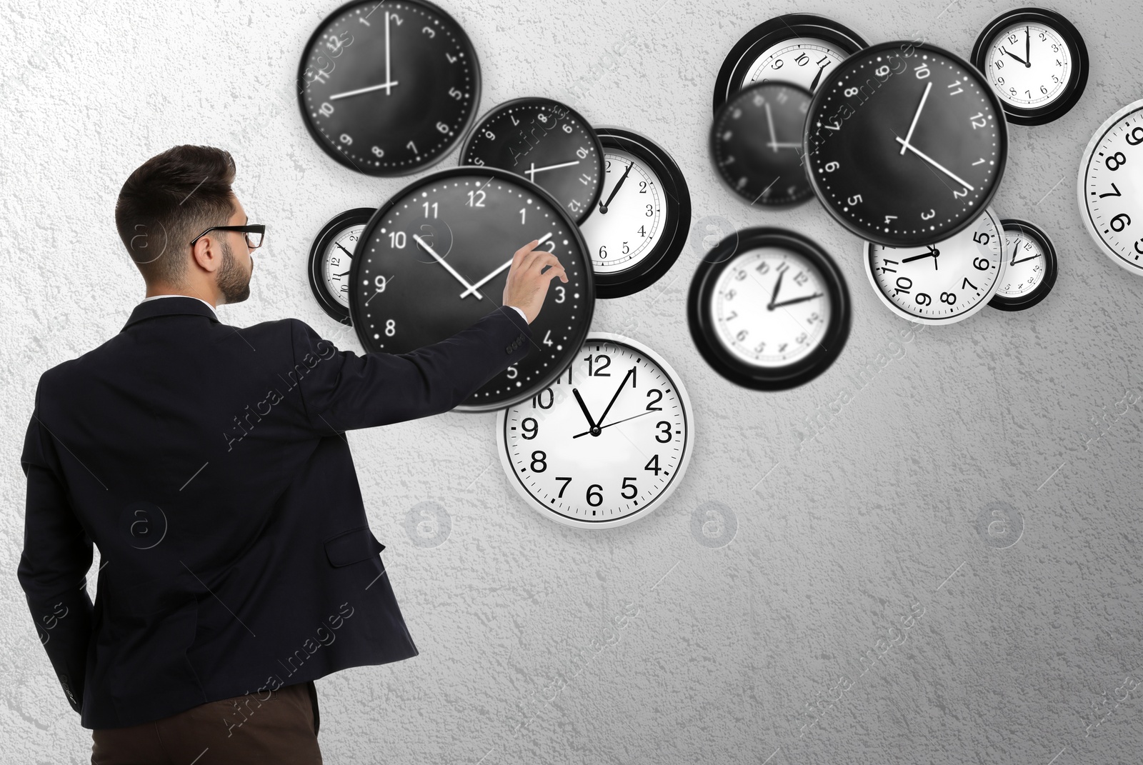 Image of Time management concept. Businessman and different clocks on light grey background