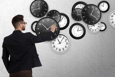 Time management concept. Businessman and different clocks on light grey background