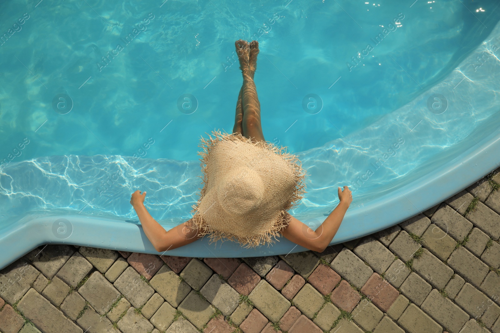 Photo of African American woman with straw hat resting in outdoor swimming pool on sunny summer day, top view