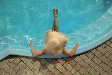 Photo of African American woman with straw hat resting in outdoor swimming pool on sunny summer day, top view