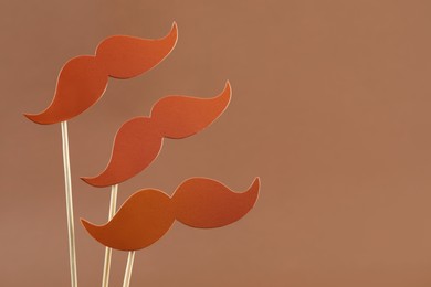 Photo of Fake paper mustaches party props on light brown background, space for text