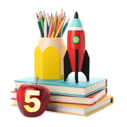 Image of Apple with carved number five as grade. Bright toy rocket and school supplies on white background