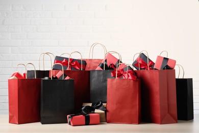 Photo of Many shopping bags with gift boxes on table against white brick wall. Black Friday sale