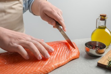 Photo of Man cutting raw salmon at grey table, closeup