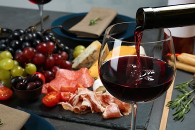 Photo of Pouring red wine into glass on served table, closeup. Space for text