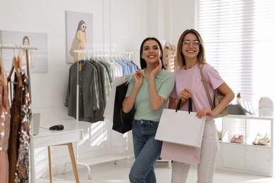 Photo of Young women with shopping bags choosing clothes in modern boutique, space for text