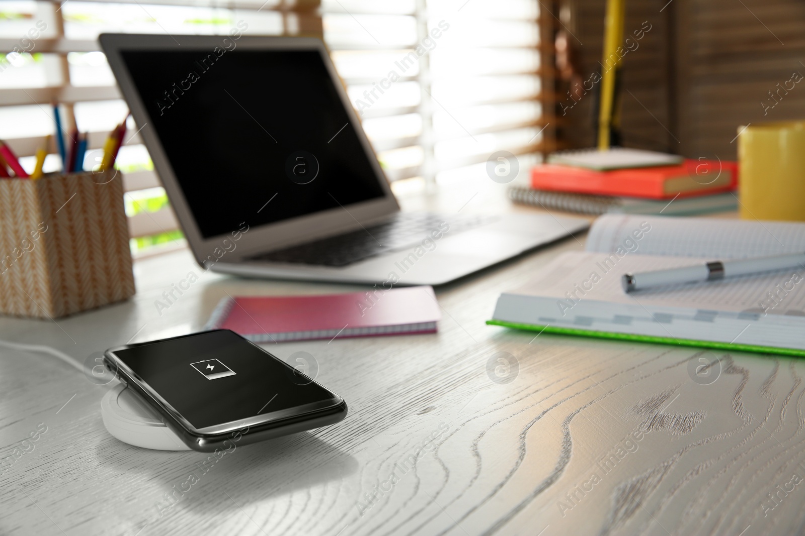 Photo of Mobile phone with wireless charger on white wooden table. Modern workplace accessory