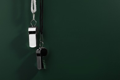 Photo of Referee equipment. Metal whistles on dark green background, closeup and space for text