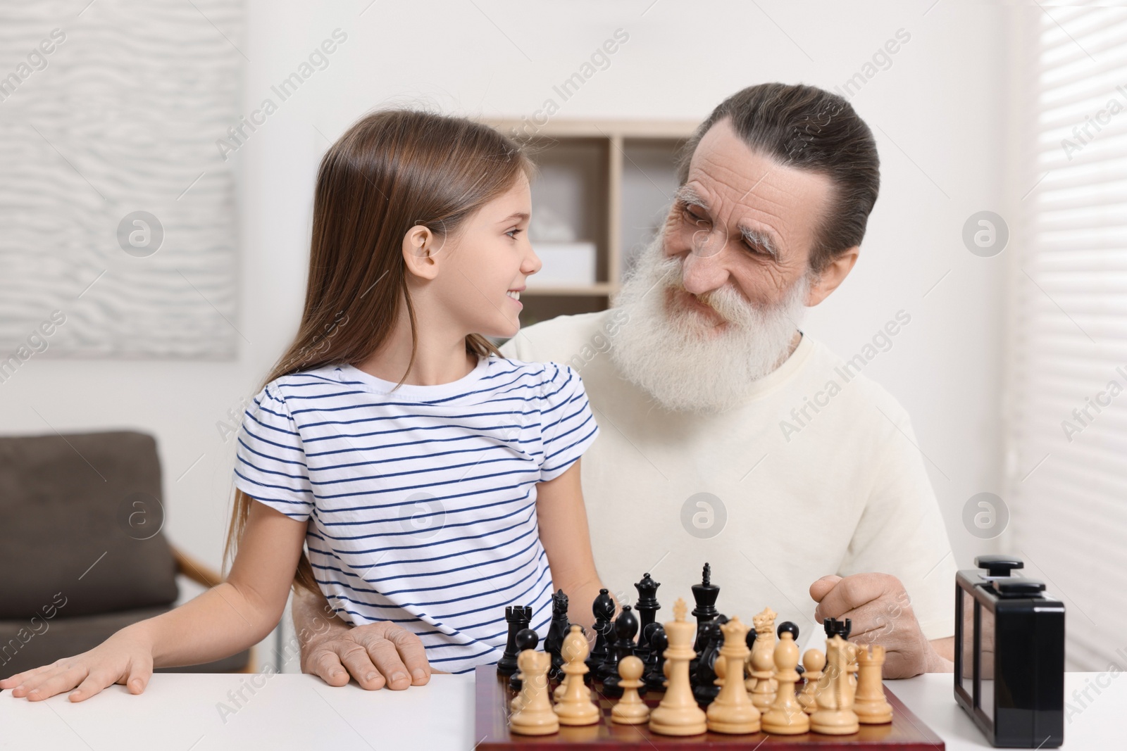 Photo of Senior man teaching his granddaughter to play chess at home