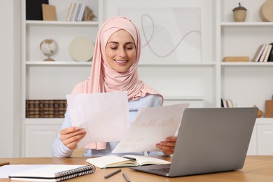 Muslim woman working near laptop at wooden table in room