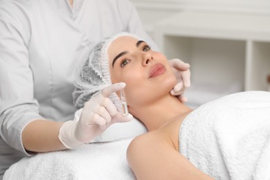 Photo of Professional cosmetologist holding skincare ampoule while working with client in clinic, closeup