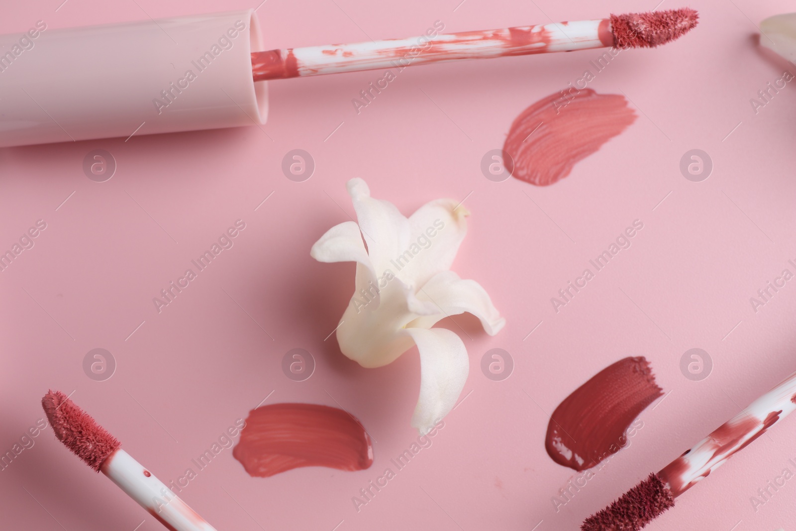 Photo of Different lip glosses, applicators and flower on pink background, flat lay