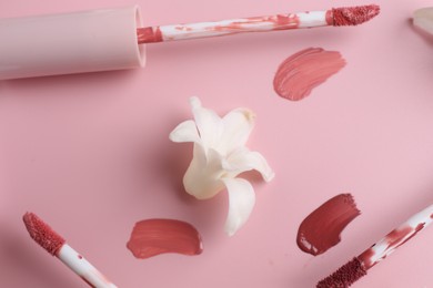 Different lip glosses, applicators and flower on pink background, flat lay