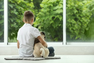 Photo of Boy with his cute pug near window indoors, back view. Space for text