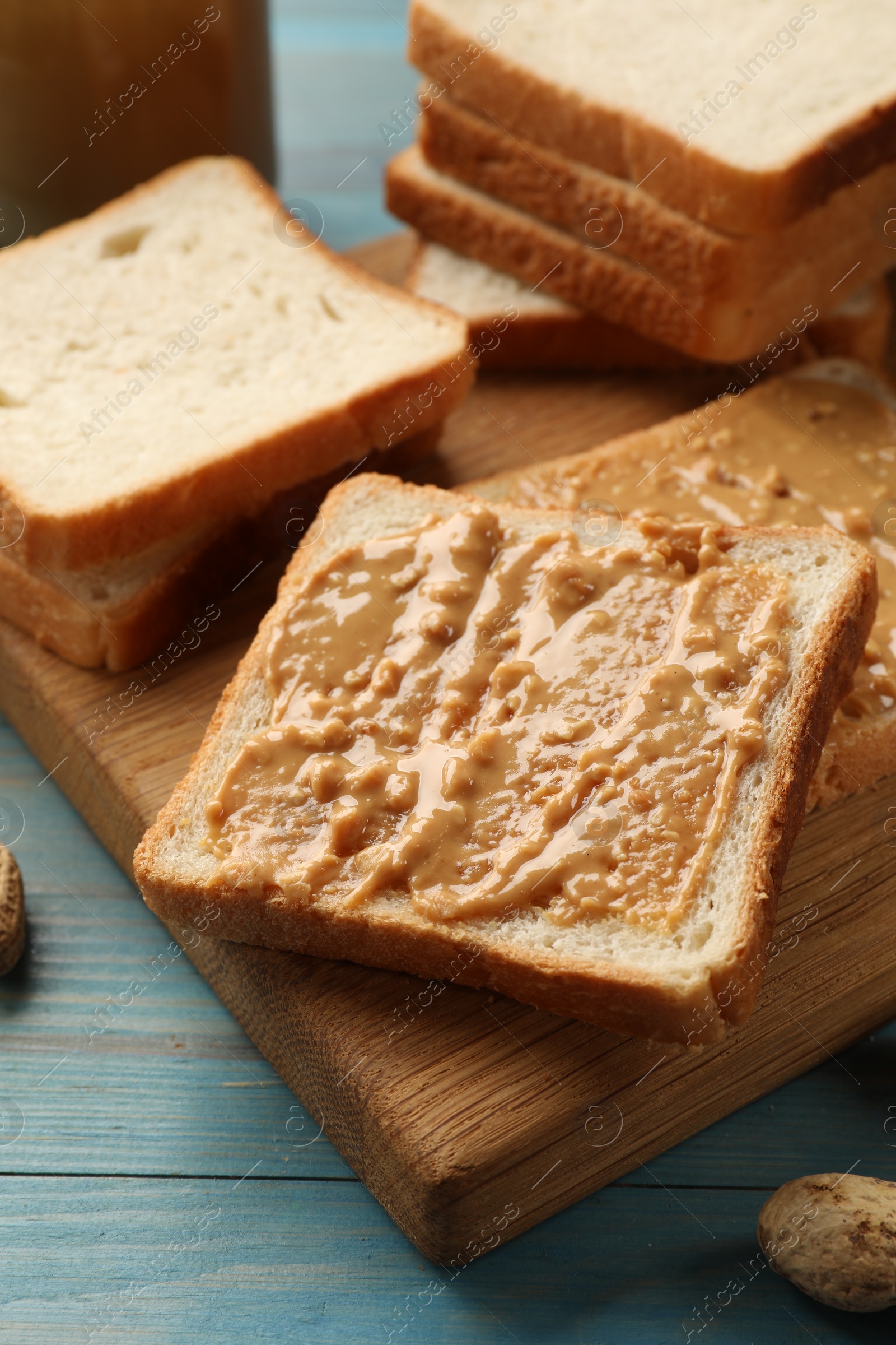 Photo of Delicious toasts with peanut butter on light blue wooden table