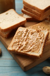 Photo of Delicious toasts with peanut butter on light blue wooden table