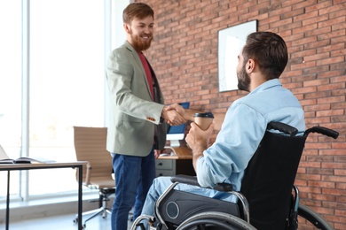 Young man in wheelchair with colleague at office