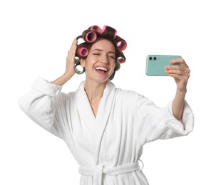 Photo of Happy young woman in bathrobe with hair curlers taking selfie on white background