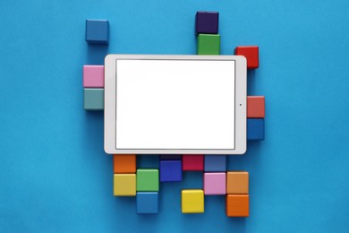 Photo of Modern tablet and cubes on light blue background, flat lay. Space for text