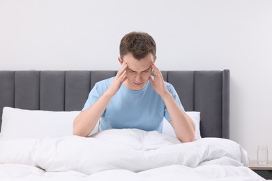 Photo of Sad man suffering from headache in bed indoors