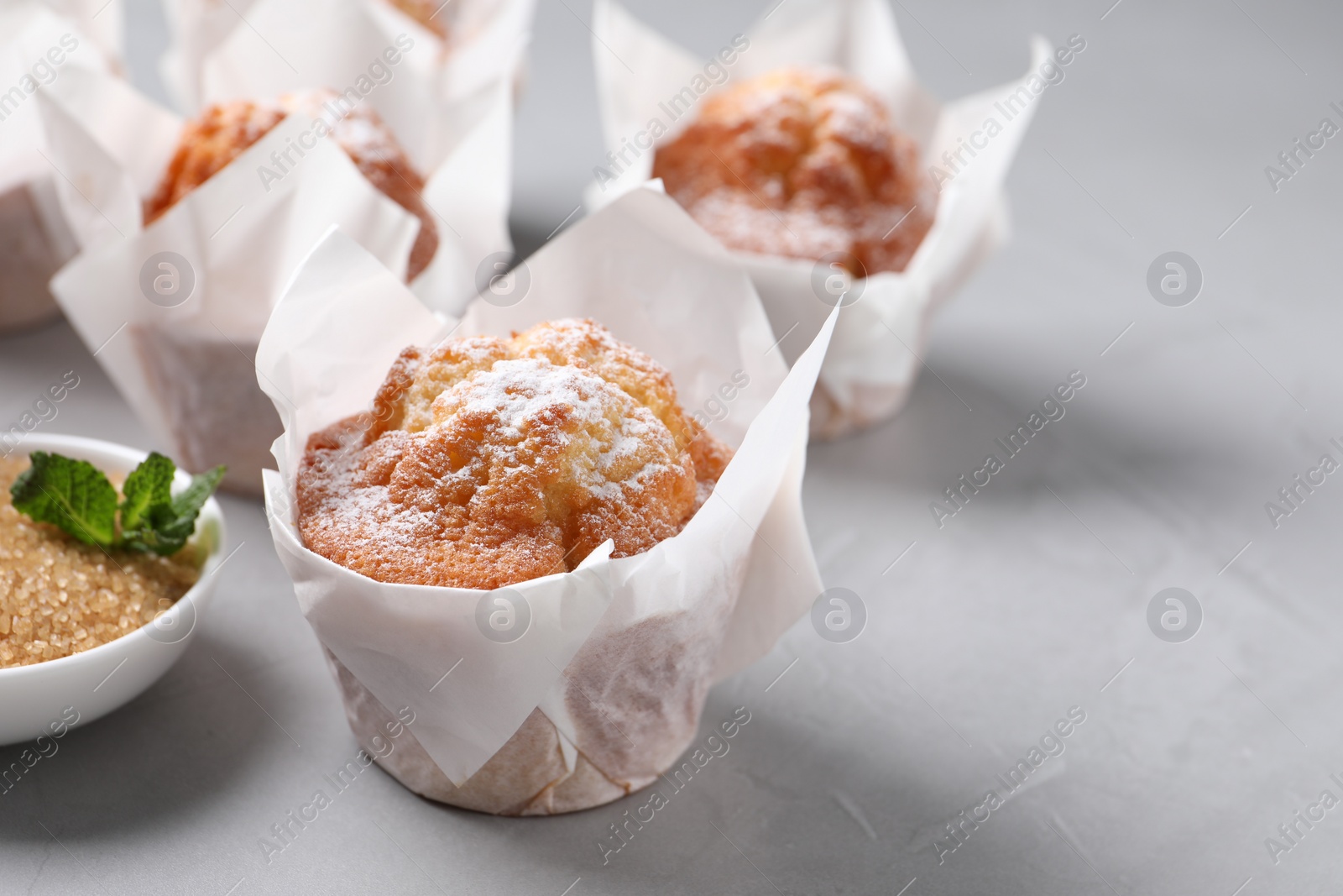 Photo of Delicious muffins with powdered sugar on grey table, closeup