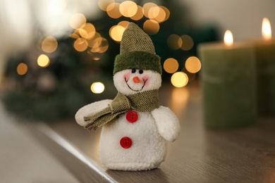 Snowman toy on table against blurred festive lights, closeup. Christmas decoration