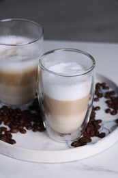 Photo of Aromatic latte macchiato and coffee beans on white marble table, closeup