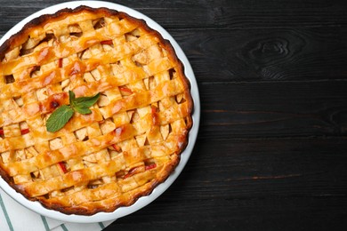 Photo of Traditional apple pie with mint on black wooden table, top view. Space for text