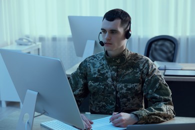 Photo of Military service. Young soldier in headphones working at table in office