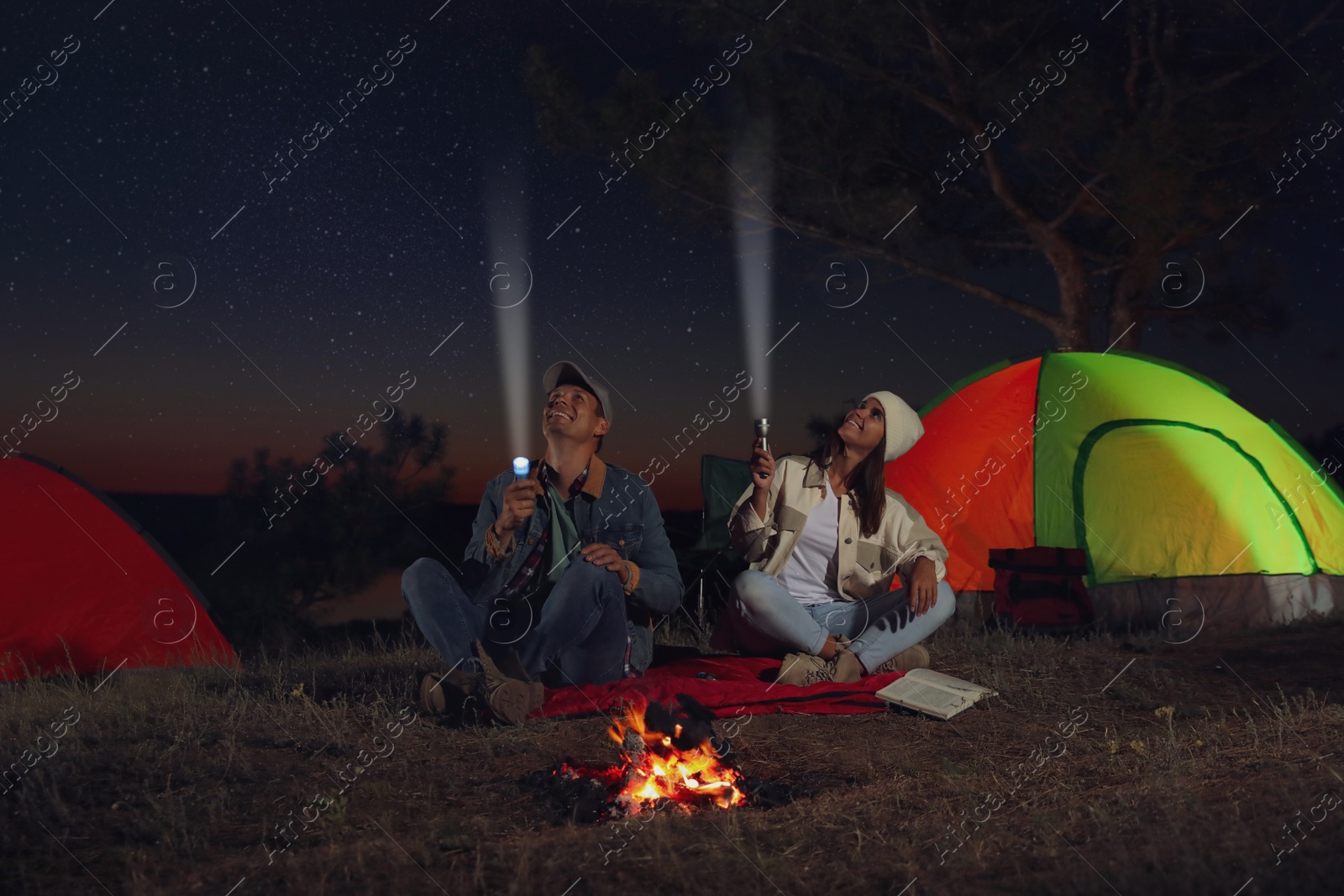 Photo of Couple with flashlights near bonfire at night. Camping season